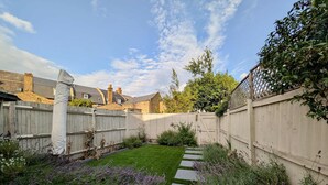 Un jardin à l’arrière de la maison, avec une clôture en bois, un chemin pavé et des plants de lavande.
