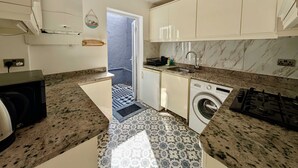 A compact kitchen with a washing machine, a stove, and a sink. - Charming House With Balcony Near Brighton Beach (Brighton)