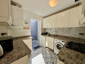 A compact kitchen with a washing machine, a stove, and a sink. - Charming House With Balcony Near Brighton Beach (Brighton)