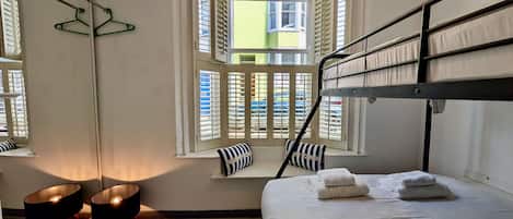 A room with a bunk bed, a window with shutters, a mirror, and a hanging light fixture.