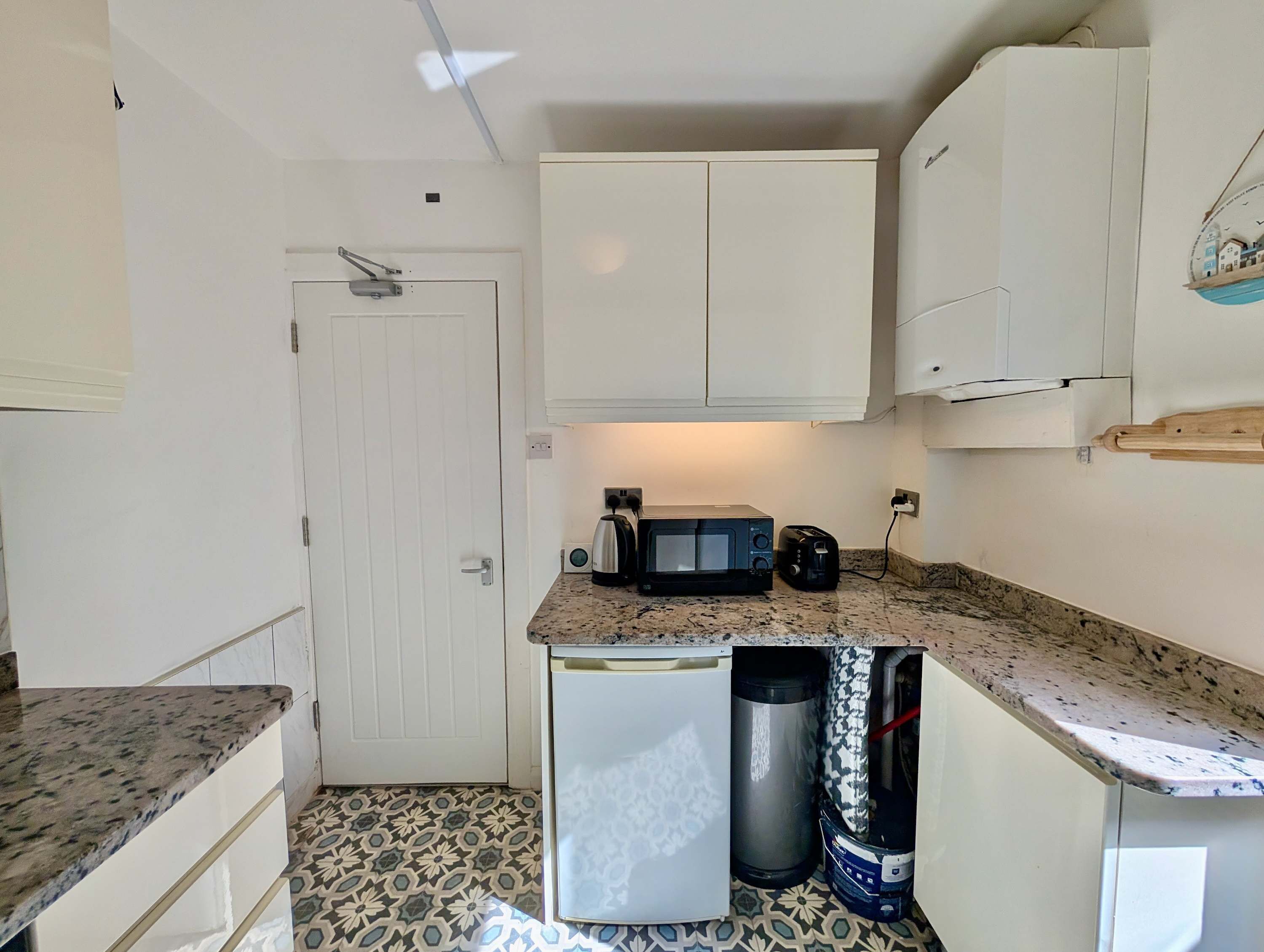 A compact kitchen with white cabinets, a microwave, a toaster, and a small refrigerator.