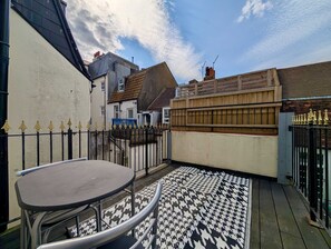 A courtyard with a metal table and chairs, a patterned floor, and a wooden fence. - Charming House With Balcony Near Brighton Beach (Brighton)