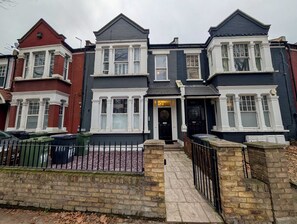 A two-story townhouse with a black and white facade, a black front door, and a number '108' above the entrance. - Stylish 2 Bed Clapham Flat With Private Patio (London)
