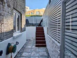 A narrow outdoor corridor with a brick wall on one side and a white wall with horizontal slats on the other. There are steps leading up to a door at the end of the corridor. - Stunning London Apartment With Private Patio (London)