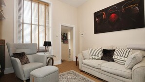 Een woonkamer met een grijze fauteuil, een beige bank en een groot abstract schilderij aan de muur.