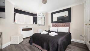 A modern bedroom with a large bed, a mirror, a white dresser, and a small ottoman. - Luxury Chelsea Flat Near Museums (London)