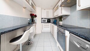 A modern kitchen with white cabinets, a black countertop, and a built-in dishwasher. - Luxury Chelsea Flat Near Museums (London)