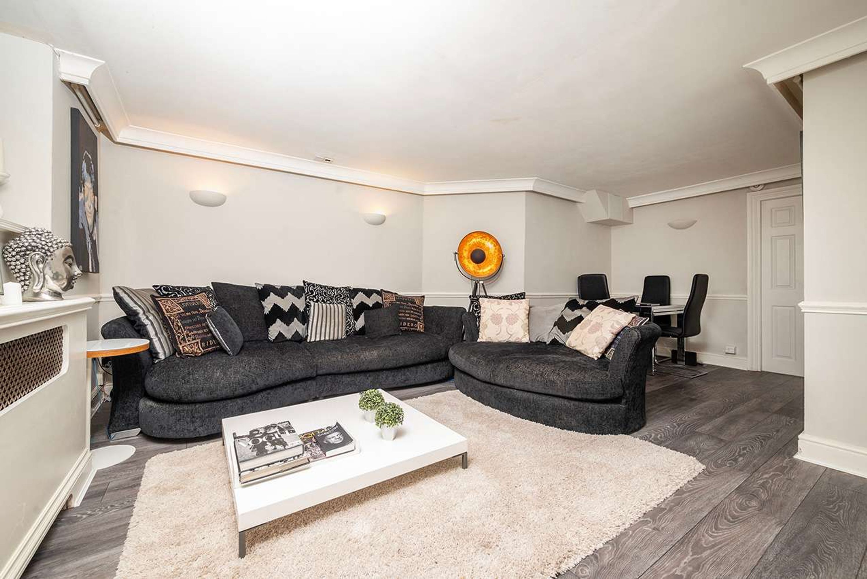 Ein modernes Wohnzimmer mit einem dunkelgrauen Ecksofa, einem weißen Couchtisch und einer dekorativen Sonnenlampe.
