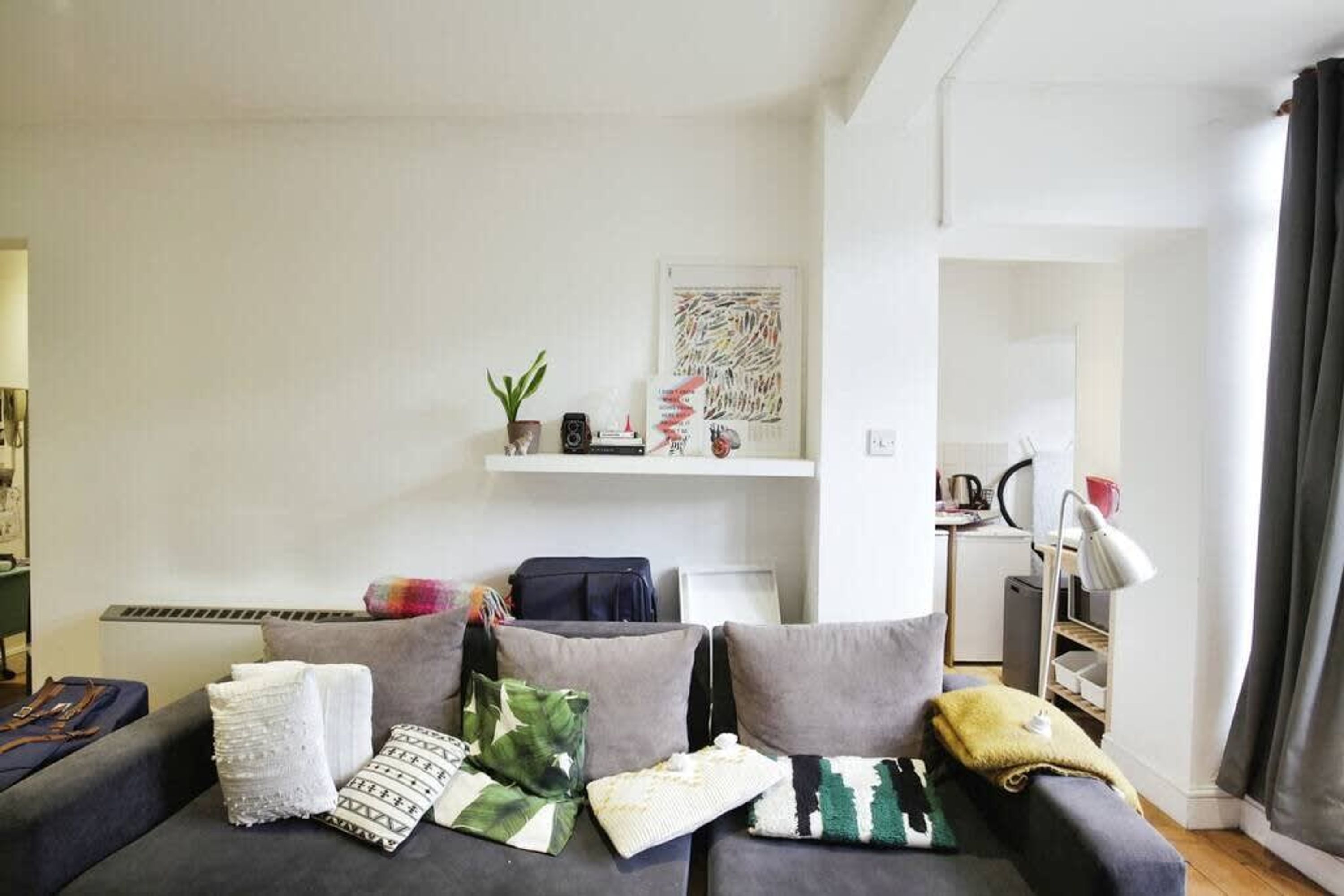 A modern living room with a grey sofa, a small plant, and a shelf with decorative items.