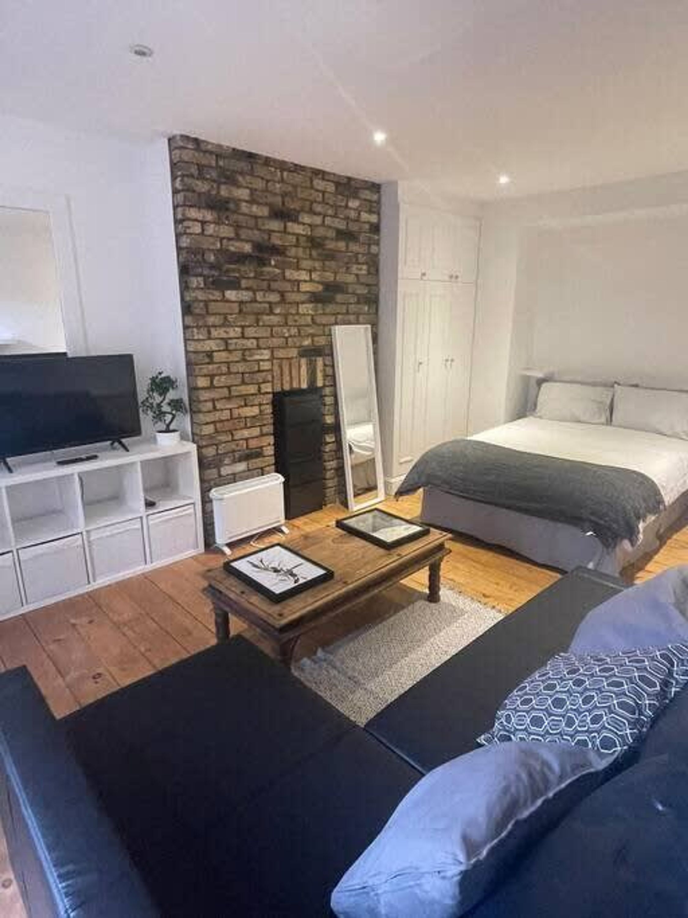 Un dormitorio moderno con una pared de ladrillo decorativa, una cama grande, un televisor y una mesa de centro de madera.