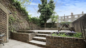 A brick patio with steps leading to a garden area, surrounded by a brick wall and a tree. - Cozy Studio With Private Garden in London (London)