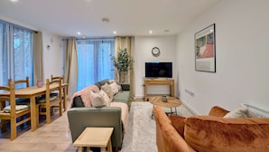 En moderne stue med sofa, fjernsyn, spisebord med stole og et lille sofabord.