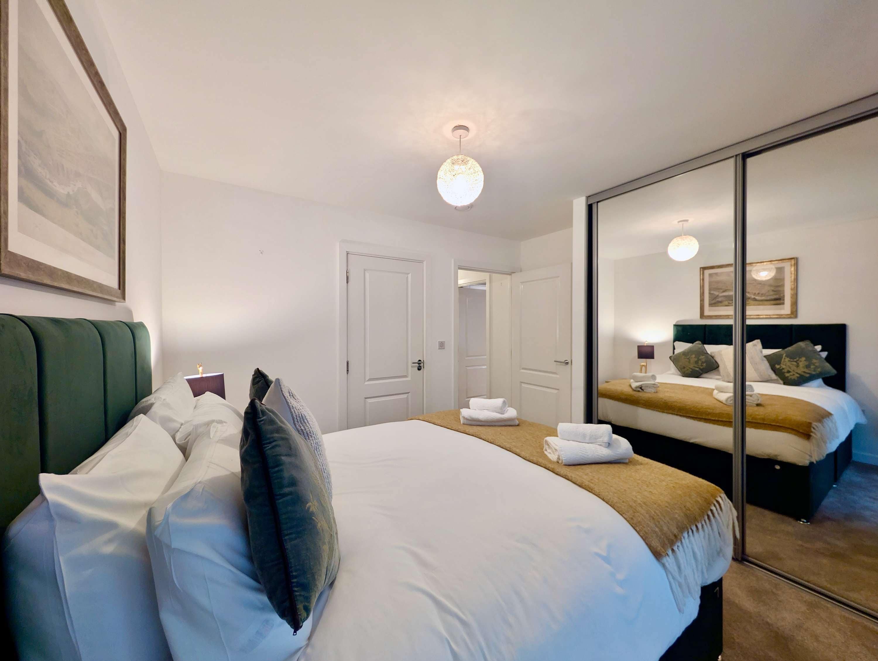 A hotel room with a large bed, a mirror, and a door leading to another room.
