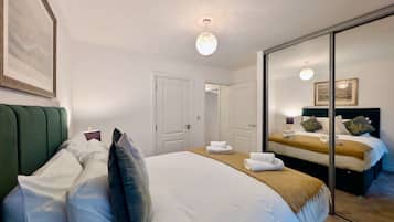 A hotel room with a large bed, a mirror, and a door leading to another room.