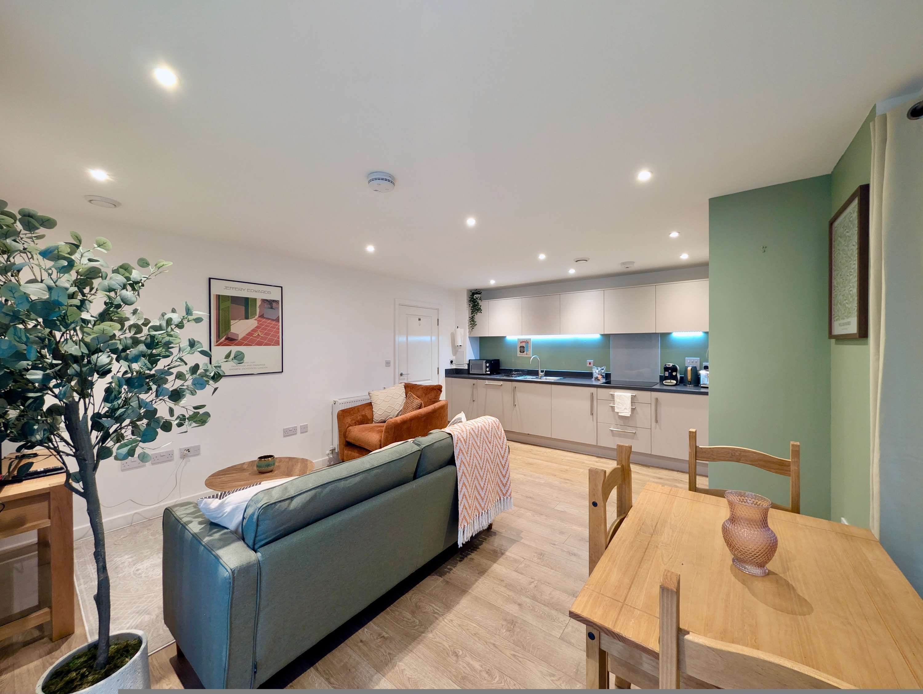 A modern living room with a sofa, a dining table, and a kitchen in the background.
