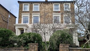 A two-story brick building with a central entrance flanked by brick walls and a black metal gate. - Victoria Park Retreat Stylish 2 Bed Flat (London)