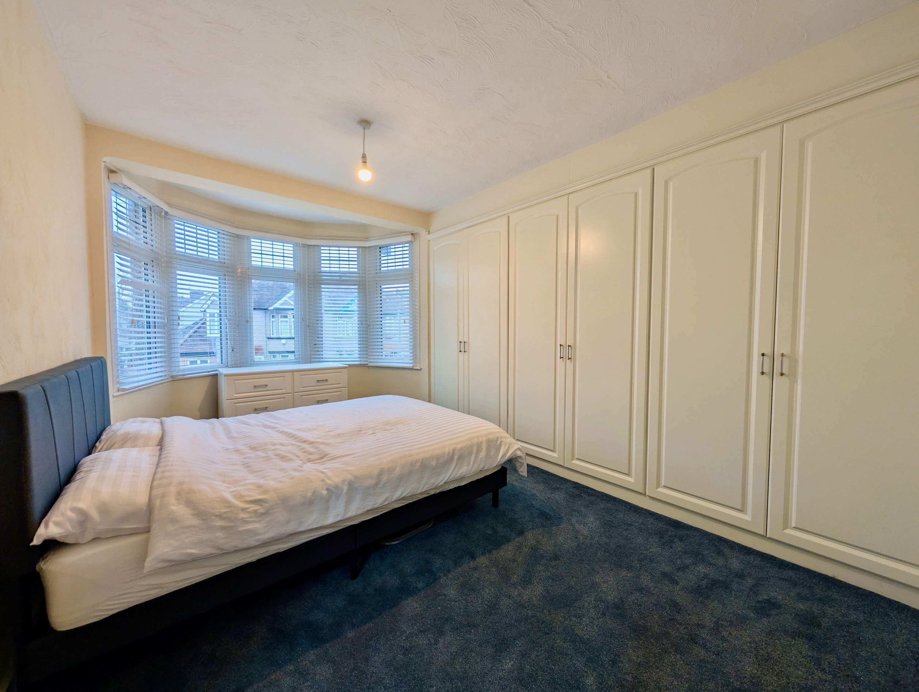 Ein Schlafzimmer mit einem Bett, einem Kleiderschrank und einem Fenster mit Jalousien.