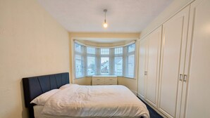 Quarto com cama, janela com persianas, guarda-roupa e uma luminária no teto.
