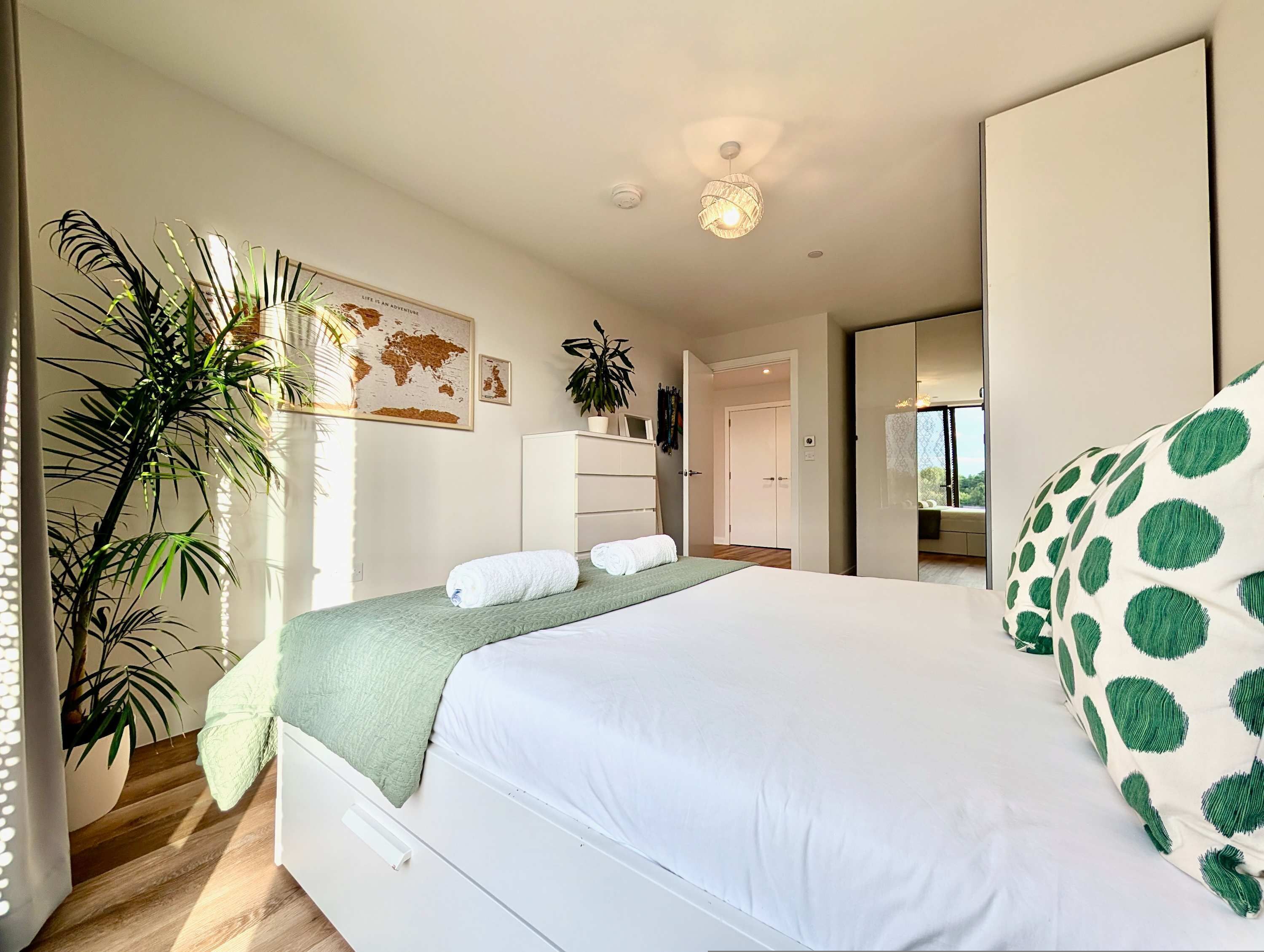 A modern bedroom with a large bed, a wardrobe, a desk, and a potted plant.