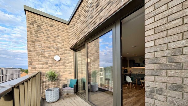 A balcony with a wooden floor, a wicker chair, a potted plant, and a view of the cityscape. - Amazing Flat With Free Parking and Balcony (Woking)