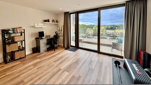 A modern living room with a large sliding glass door to a balcony, a desk with a computer, a bookshelf, and exercise equipment. - Amazing Flat With Free Parking and Balcony (Woking)