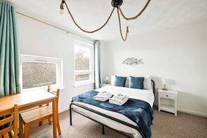 Ett sovrum med en säng, ett sängbord, en stol, ett fönster och en taklampa.