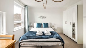 A hotel room with a bed, a desk, a wardrobe, and a view of the outside. - Spacious 5-bedroom Family Home in Greenwhich (London)