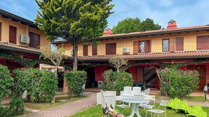 A courtyard with a brick pathway, white outdoor furniture, and a bicycle. - Terraced House Near Bibione Beach (San Michele al Tagliamento)