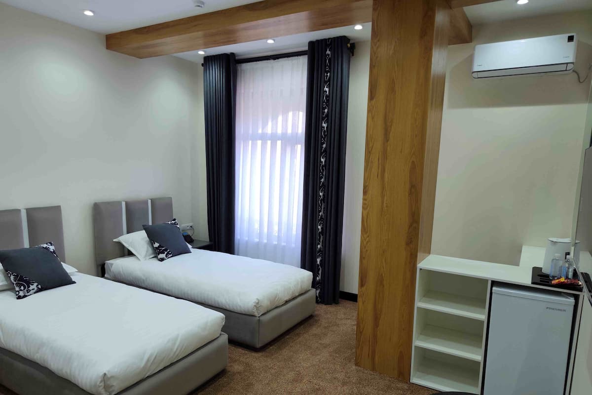 Una camera d'albergo con due letti, una scrivania, un minibar e una finestra con tende.