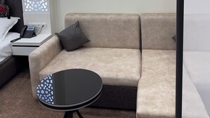 A modern hotel room with a beige sofa, a small round table, a decorative partition with a star pattern, and a bedside phone. - SHOHI ZINDA HOTEL (Samarkand)