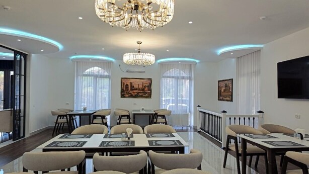 A spacious dining area with multiple tables, elegant chandeliers, and artwork on the walls. - SHOHI ZINDA HOTEL (Samarkand)