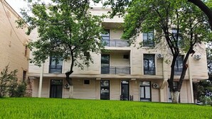 A building with a flat facade, multiple balconies, and a well-maintained lawn in front. - SHOHI ZINDA HOTEL (Samarkand)