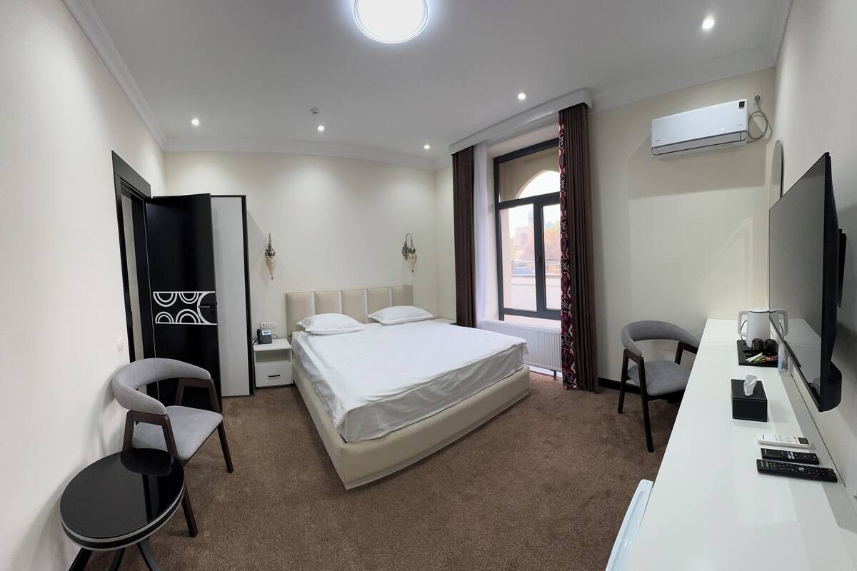 Una camera d'albergo con un letto, una scrivania, una sedia, una televisione e un condizionatore d'aria.