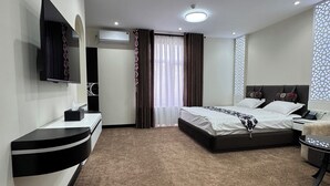A hotel room with a bed, bedside table, TV, and a desk with a chair. - SHOHI ZINDA HOTEL (Samarkand)