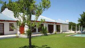A white building with a red door, a swimming pool, and a well-maintained lawn. - Rhino Creek Estate (Bloemfontein)