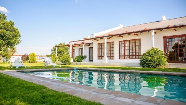 A poolside view of a house with a white exterior, red window frames, and a tiled deck. - Rhino Creek Estate (Bloemfontein)