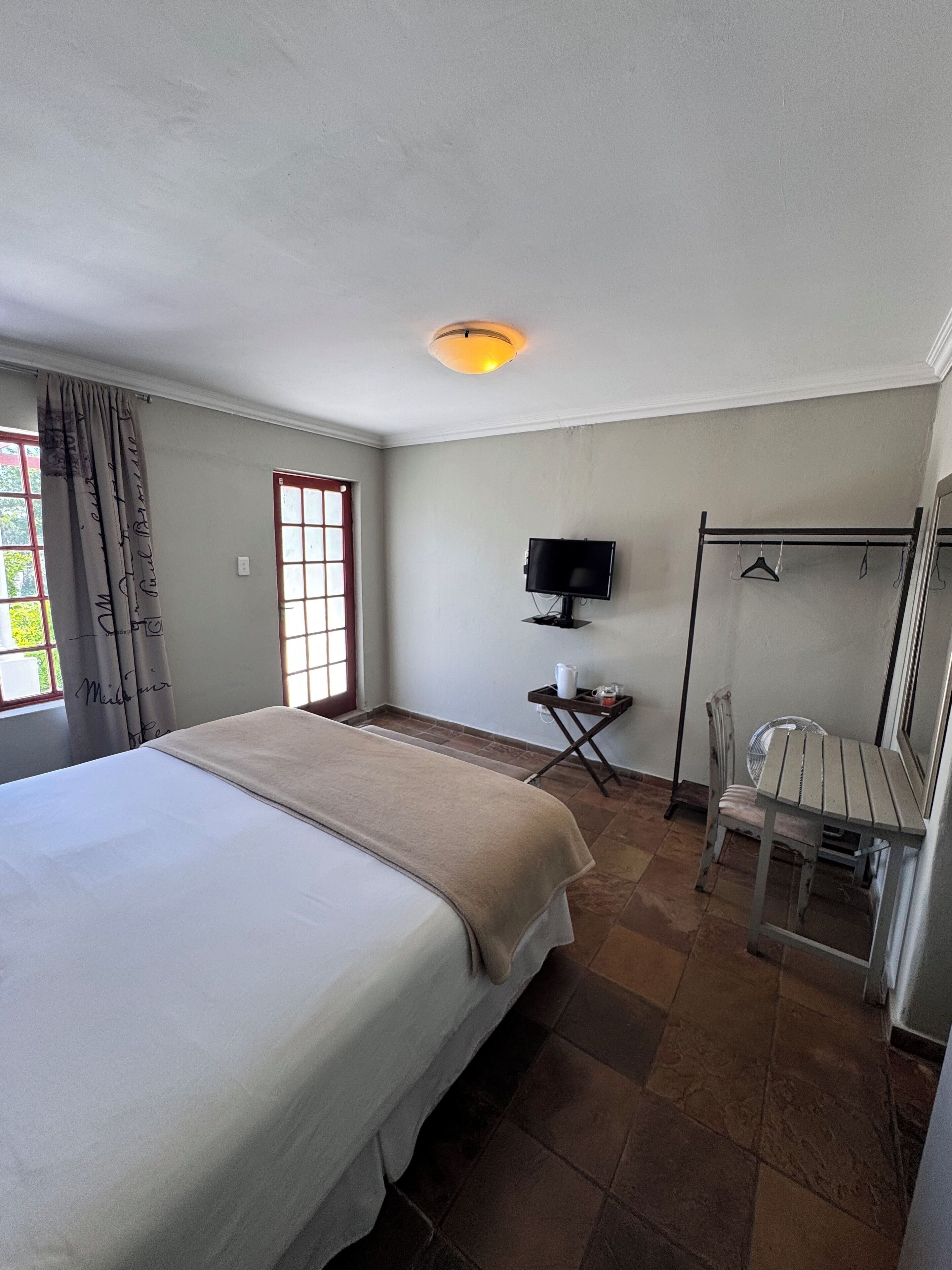 A hotel room with a large bed, a television, a small table with a fan, and a window with curtains.