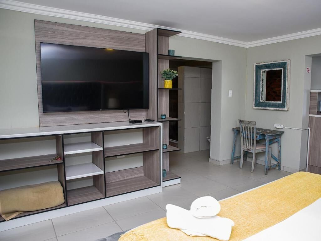 A modern living room with a flat-screen TV mounted on the wall, built-in shelving, a dining area with a table and chairs, and a small seating area with a sofa.