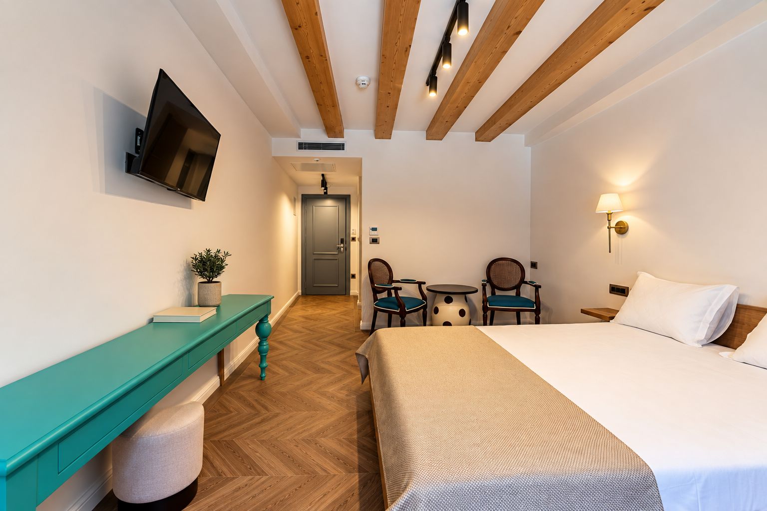 A hotel room with a bed, a desk with a chair, a television, and a small table with chairs.