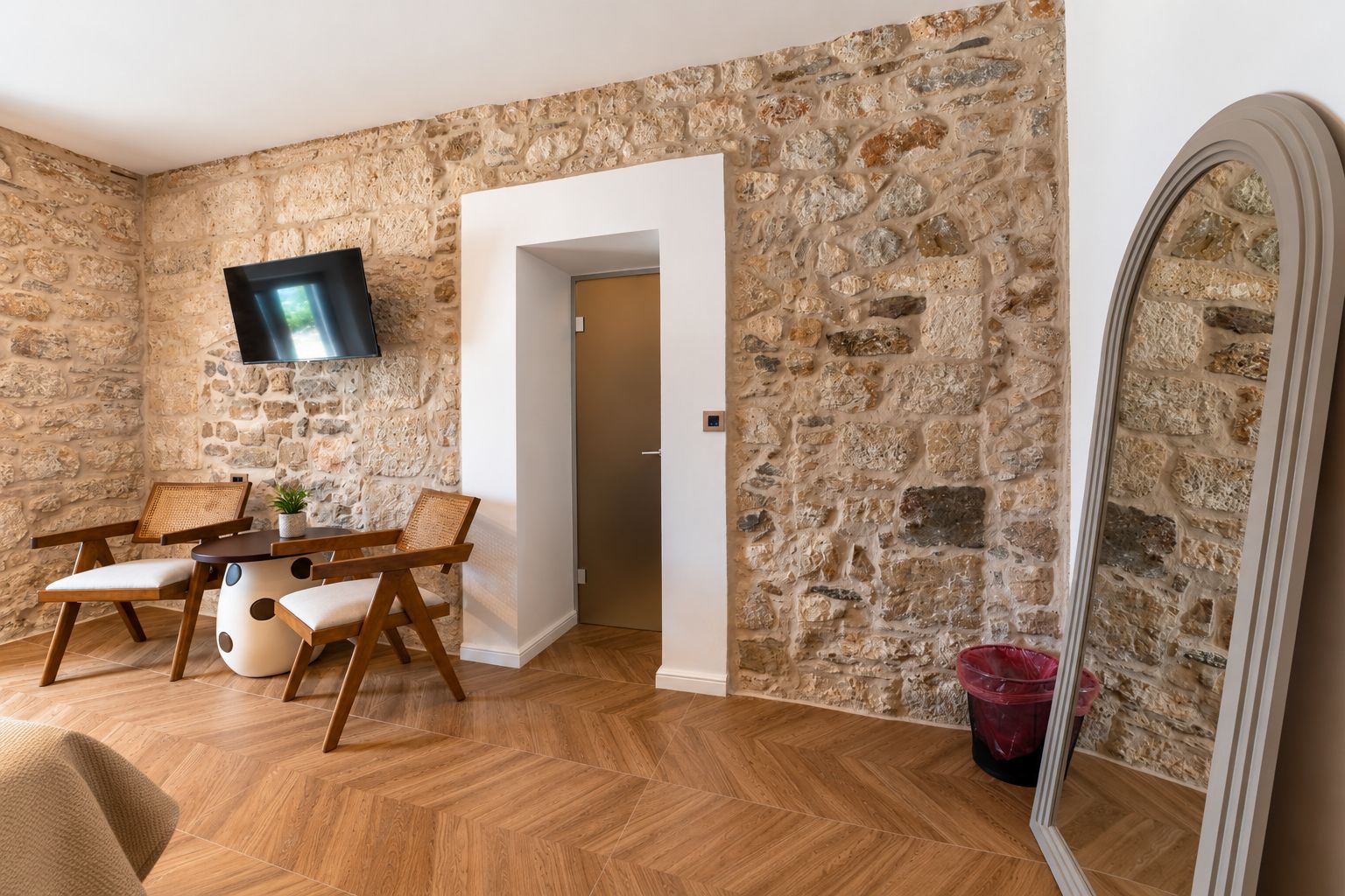 Una habitación con pared de piedra, una mesa de comedor de madera con sillas, un televisor montado en la pared y un espejo.