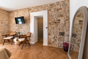 Una habitación con pared de piedra, una mesa de comedor de madera con sillas, un televisor montado en la pared y un espejo.