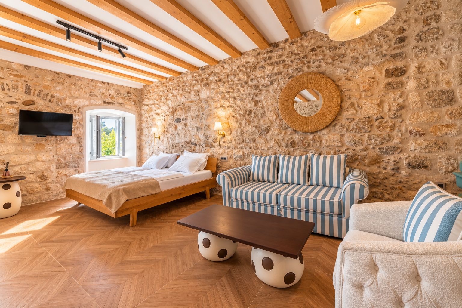 Una habitación con pared de piedra, vigas de madera, una cama, un sofá, una mesa de centro y un televisor.