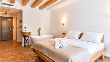 Una habitación de hotel con una cama grande, una bañera y suelo de madera.