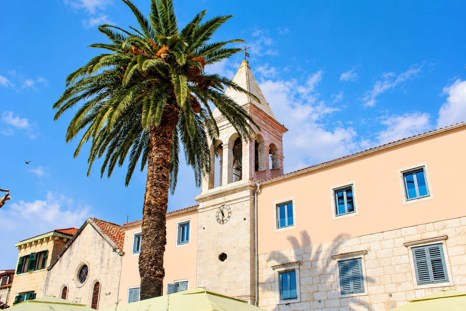 Un edifici amb una torre del rellotge, palmeres i un cel blau clar.