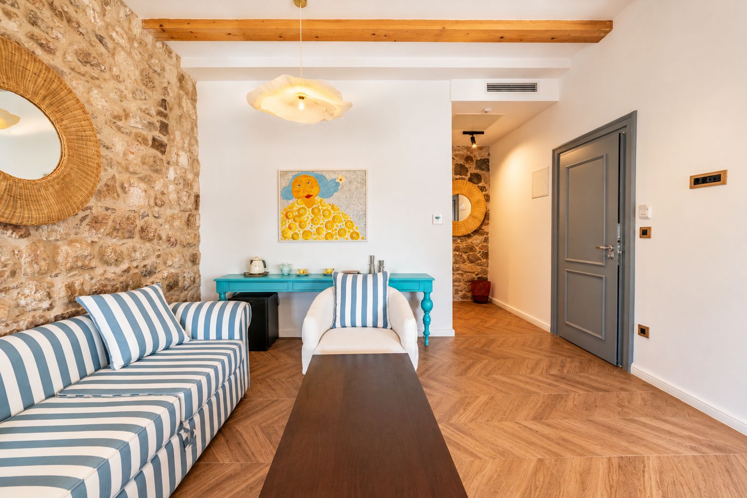A room with a stone wall, a sofa with striped cushions, a wooden dining table, and a door.