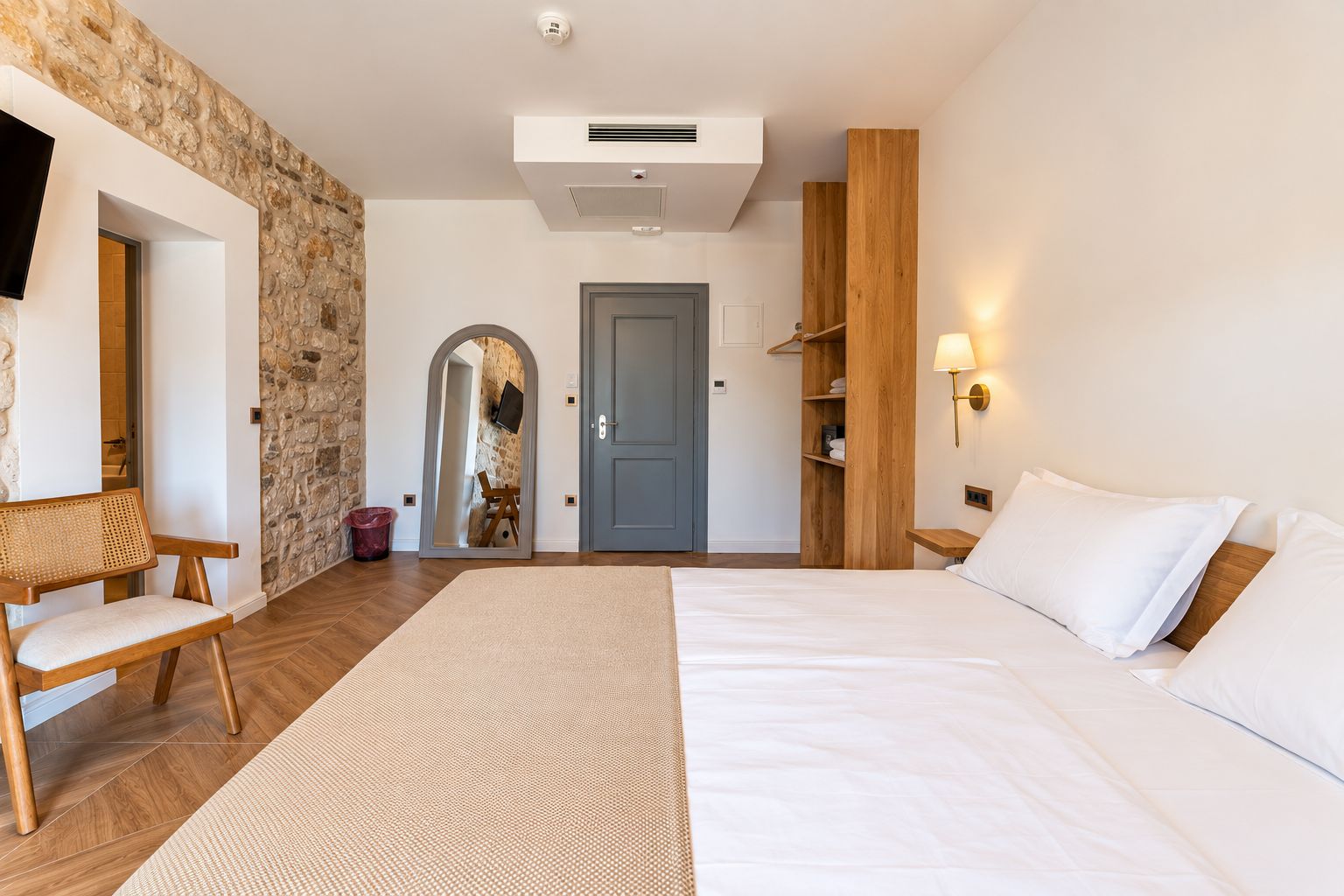 A bedroom with a bed, a wooden bench, a stone wall, a door, and a mirror.