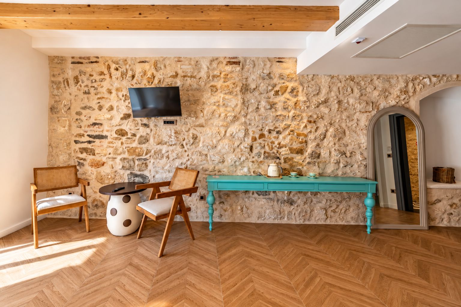 A room with a stone wall, wooden furniture, a teal table, and a flat-screen TV mounted on the wall.