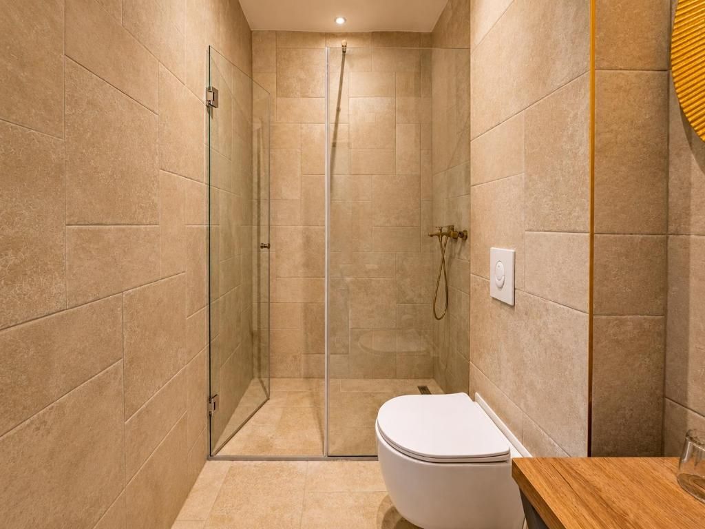 Un baño con ducha envuelta en cristal, inodoro blanco y encimera de madera.