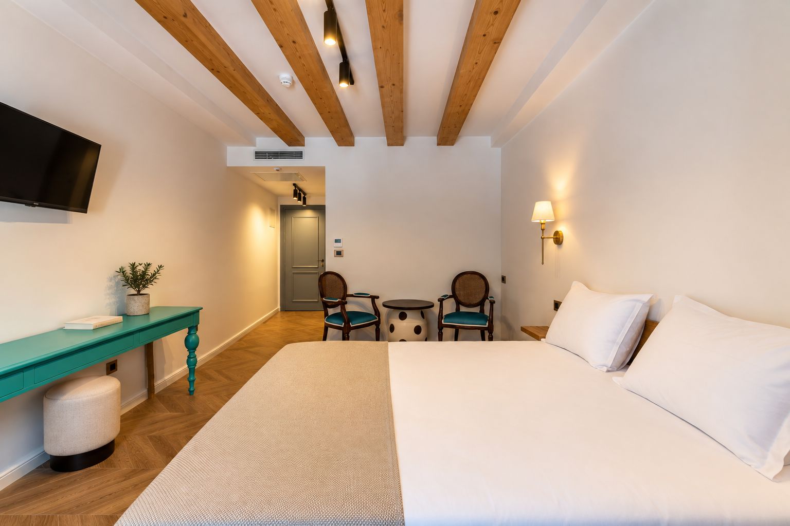 Una habitación de hotel con cama, escritorio, dos sillas, televisor y lámpara.