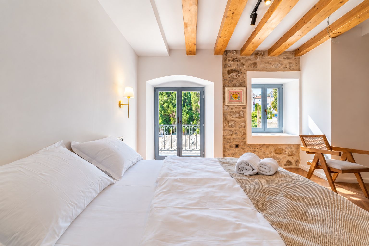 Un dormitorio con cama, ventana, pared de piedra y balcón.